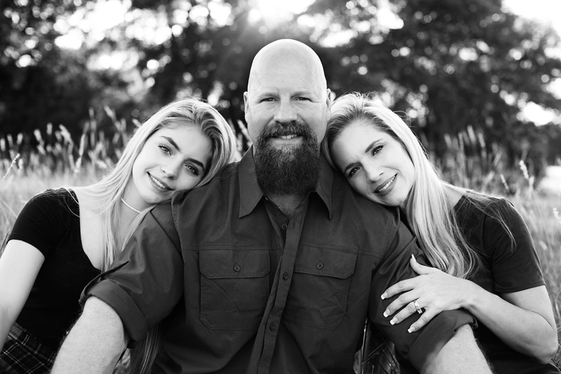 Family Photographer, a father sits as his two teen daughters lean on him tenderly