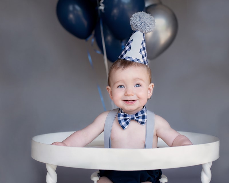 Baby Photography, A boy sits up smiling with balloons and a party hat attached
