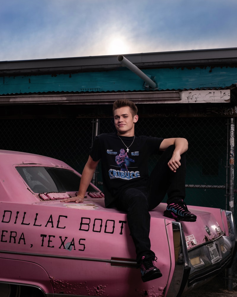 Senior Photographer, high school boy sits on the trunk of an old pink cadillac