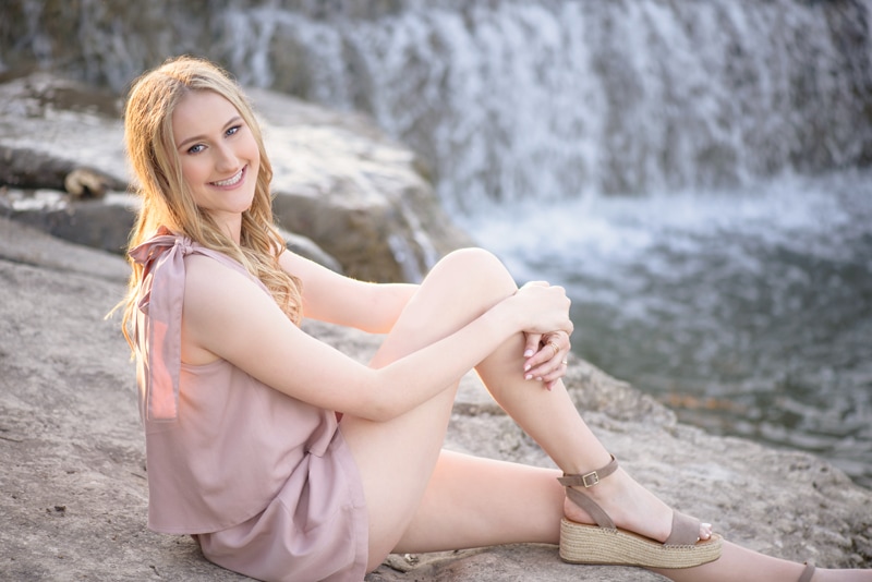 Senior Photographer, a teenage woman sits on the rocks near a waterfall