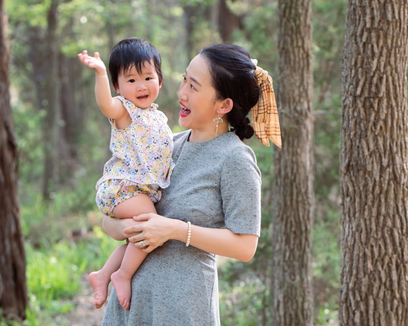 milestone photography, happy mother stands in the forest carrying baby daughter