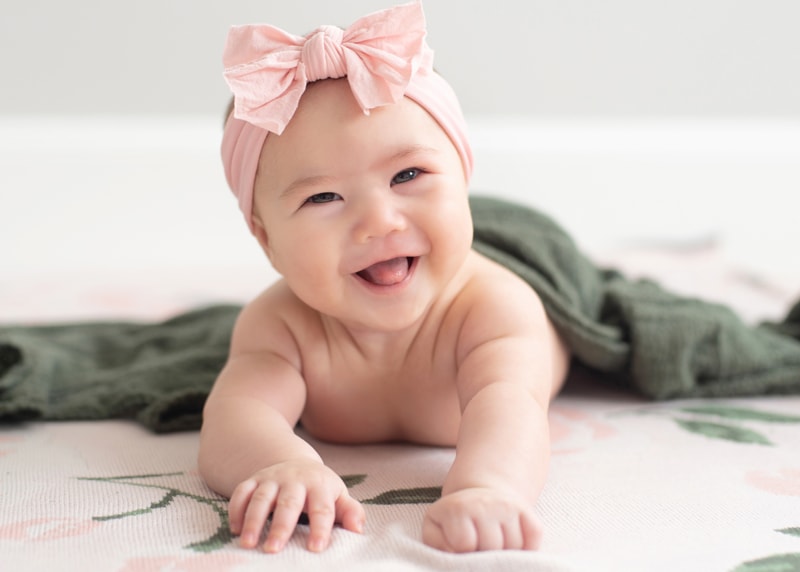 milestone photography, a baby girl sits on her stomach smiling with bow in her hair