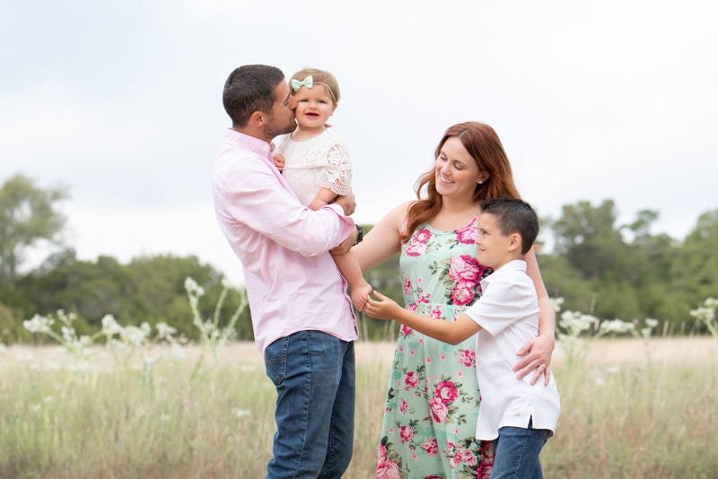 milestone photography, a mother and father love on their baby daughter and young son in an open field