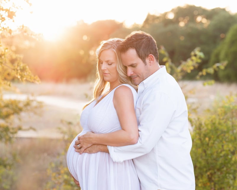 Maternity Photographer, husband and wife embrace holding onto mothers belly outdoors