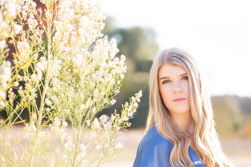 Senior Photographer, a high school girl stands gazing in a field near flowering plants