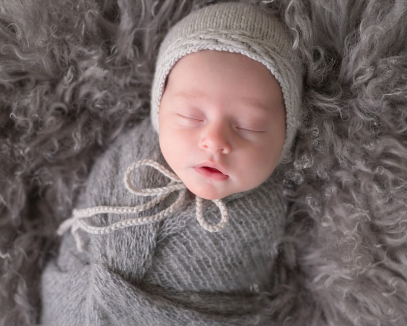 Newborn Photography, a little baby lays sleeping on a fluffy blanket swaddled in knit blankets and a beanie