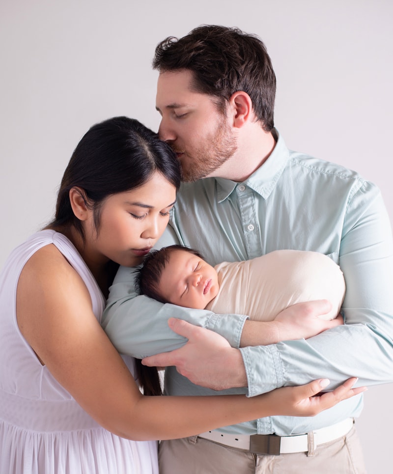 Newborn Photography, dad holds new baby as mom kisses little head