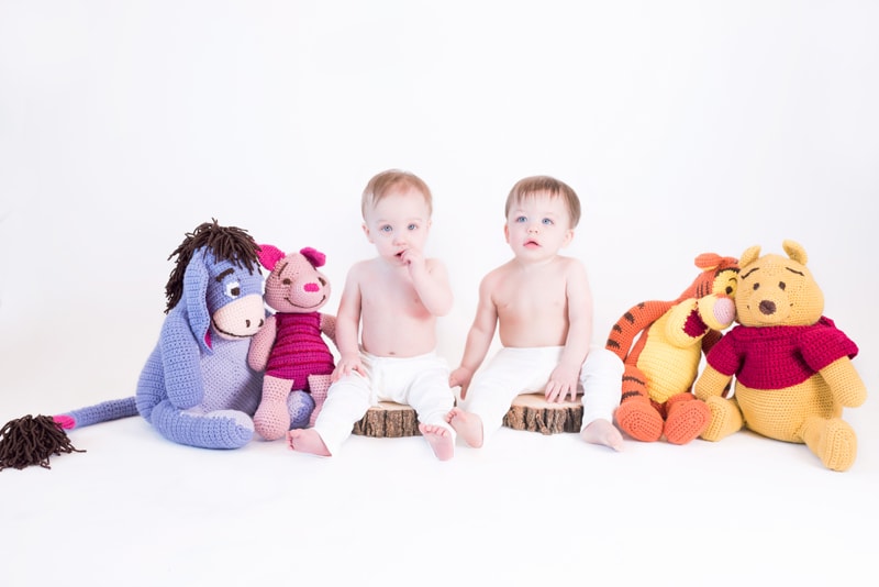 milestone photography, twins sit beside Winnie the Pooh stuffed animals in the studio