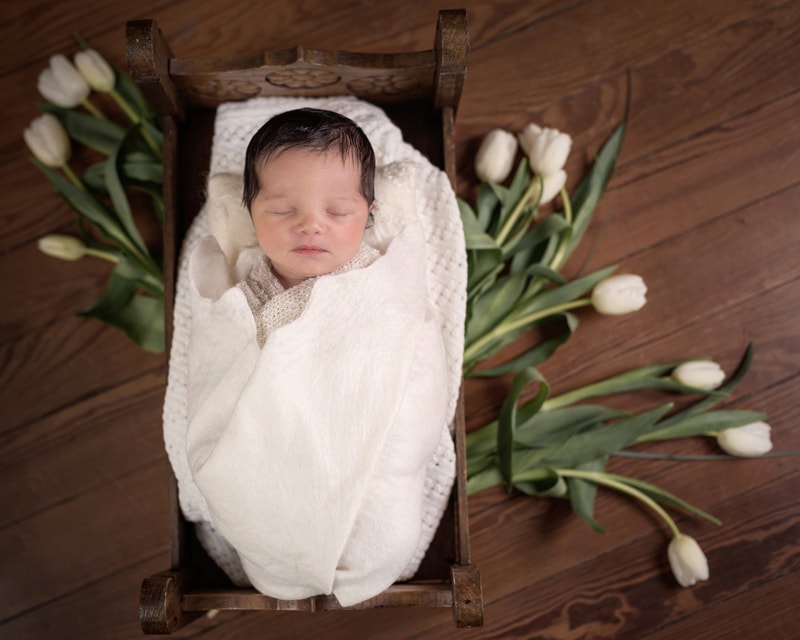 Newborn Photography, a little baby with a full head of hair lays sleeping in a small crib, tulips underneath