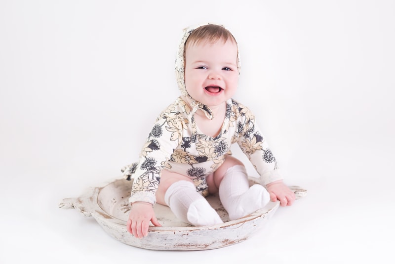 milestone photography, baby girl wearing a floral bonnet sits in a decorative cast iron dish