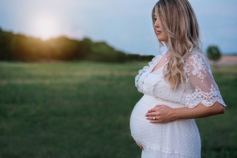 Maternity Photography, Pregnant woman wears white dress and stands in grassy field