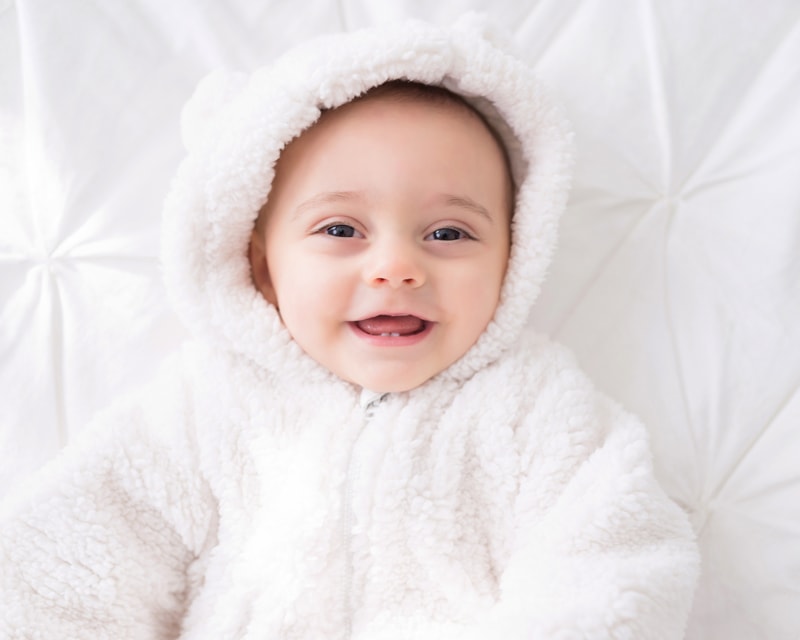 milestone photography, baby in bear pajamas smiles while laying on the bed
