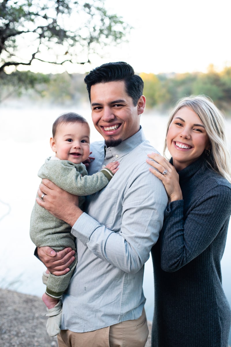 Family Photographer, two young parents hold their baby son near a quiet lake