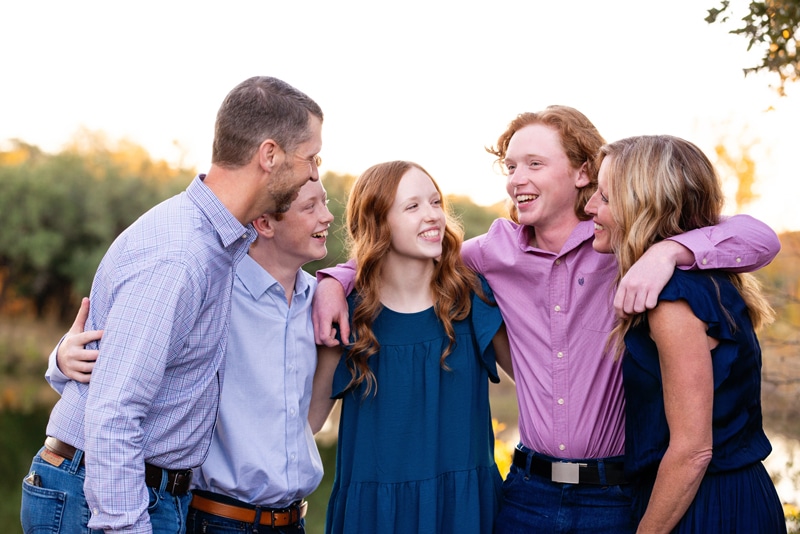 Family Photographer, a happy family of five huddles and smiles in the forest