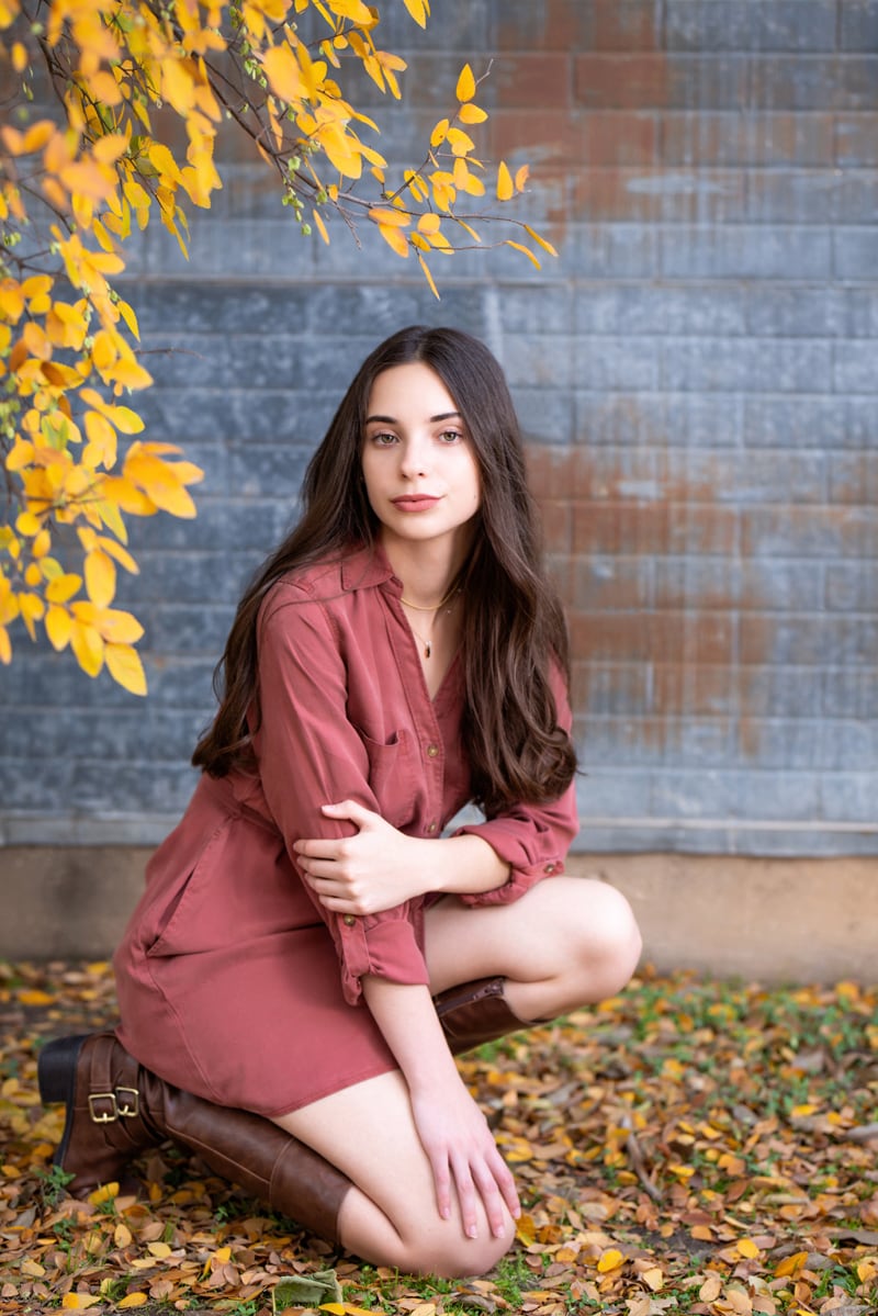 Senior Photographer, teenage girls kneels in the dry autumn leaves