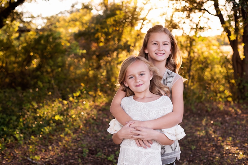 Family Photographer, two young sisters hold each other close in the forest at golden hour