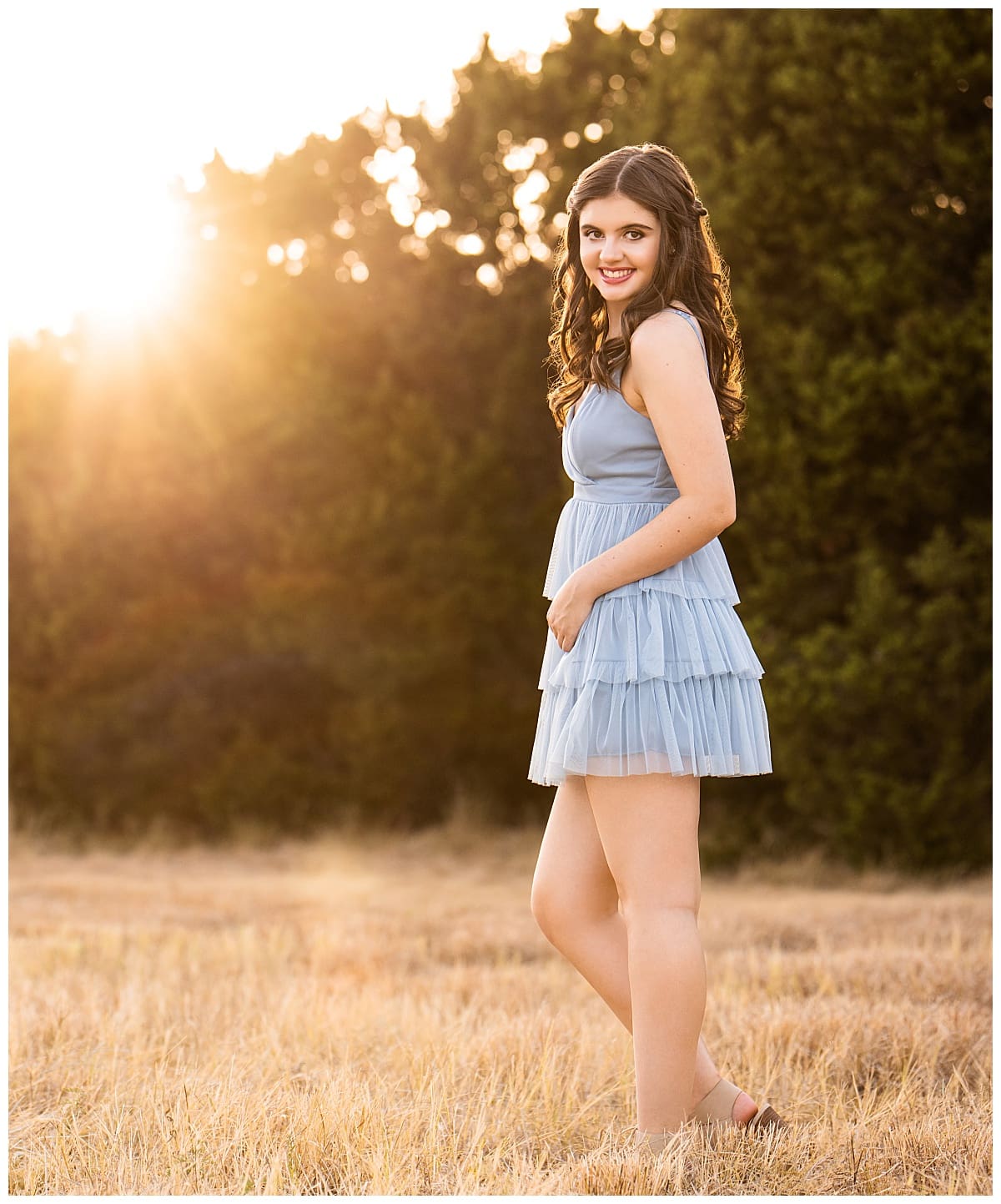 senior in blue dress stands in field for Studio + Creekside Sunset Session
